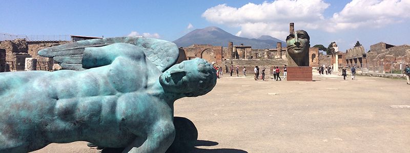 Fallen staty i ruinstaden Pompejii med vulkanen Vesuvius.